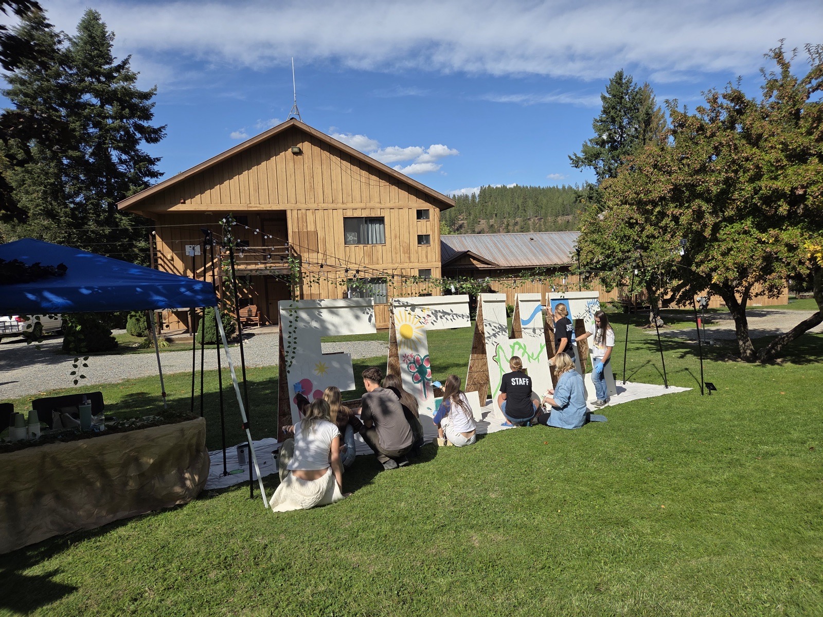 Painters sitting in the grass in front of the panels, the lodge behind