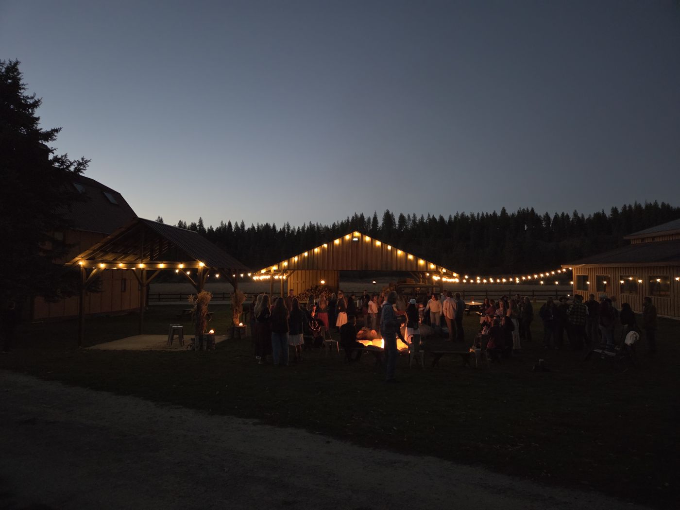 People gathered around a fire under string lights at dusk