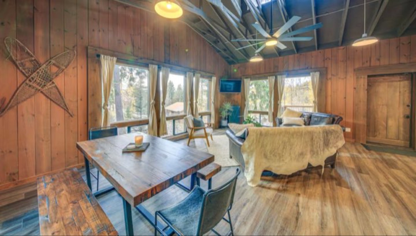 The Cedar Chalet living room, wood-paneled with big windows to the trees